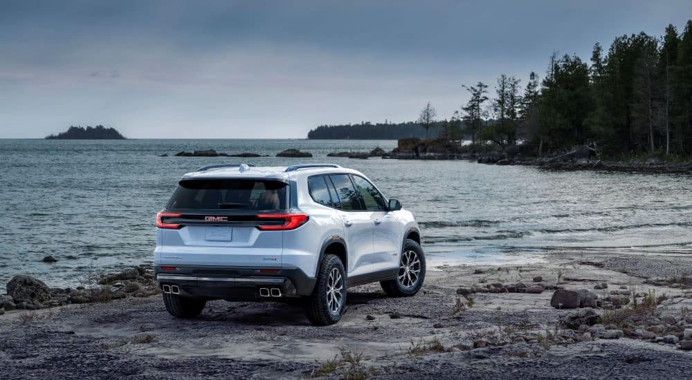 A white 2024 GMC Acadia AT4 is shown parked near a lake.